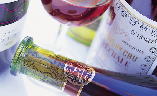 View of two wine bottle labels a glass of light red wine in the centre and a bottle laying on it's side in the centre foreground