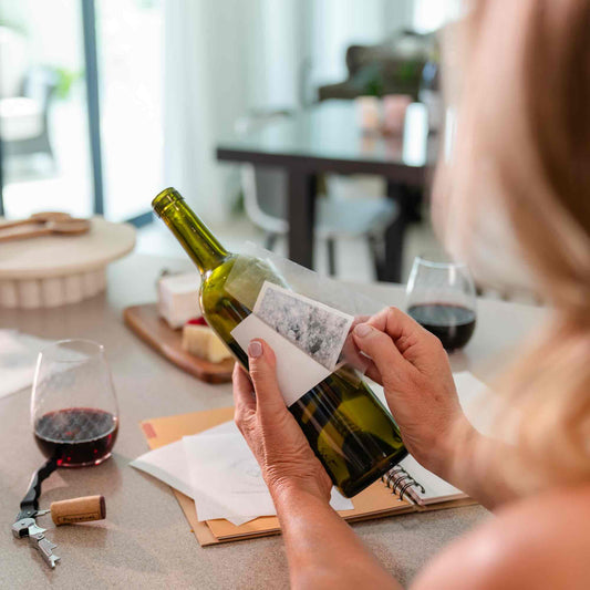 Person peeling wine bottle label away from wine bottle using wine label remover sheet